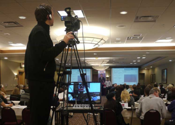 The conference attendees are currently in a meeting, with a cameraman capturing footage