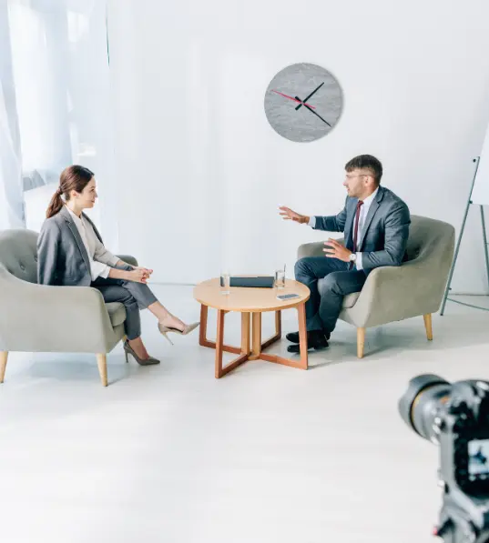 There are two artists sitting in chairs and having a conversation, which was shot with a camera.